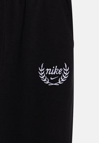 Fekete melegítőnadrág fehér hímzett Nike logóval, babérlevelek mintájával. Pamut anyag, sima felülettel és rugalmas derékkal.