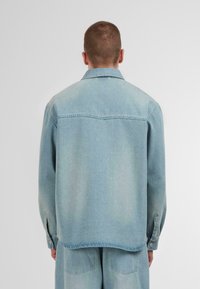 Lichtblauwe spijkerjas met een kraag, lange mouwen en knoopmanchetten. Heeft een rechte snit en minimalistisch ontwerp, zonder zichtbare patronen.
