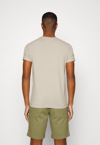 Beige kortærmet t-shirt med rund hals, glat tekstur og lige kant, parret med olivengrønne shorts.