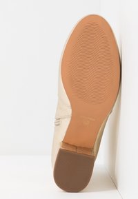 Béžová lodička na vysokém podpatku s hladkým kovovým povrchem, texturovanou stélkou a světle hnědou gumovou podrážkou, s minimálním zdobením a logem.