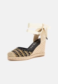 Espadrilles nere e dorate con zeppa intrecciata e tacco simile alla juta, lacci alla caviglia in tessuto beige e punta rotonda, caratterizzate da una tomaia testurizzata.