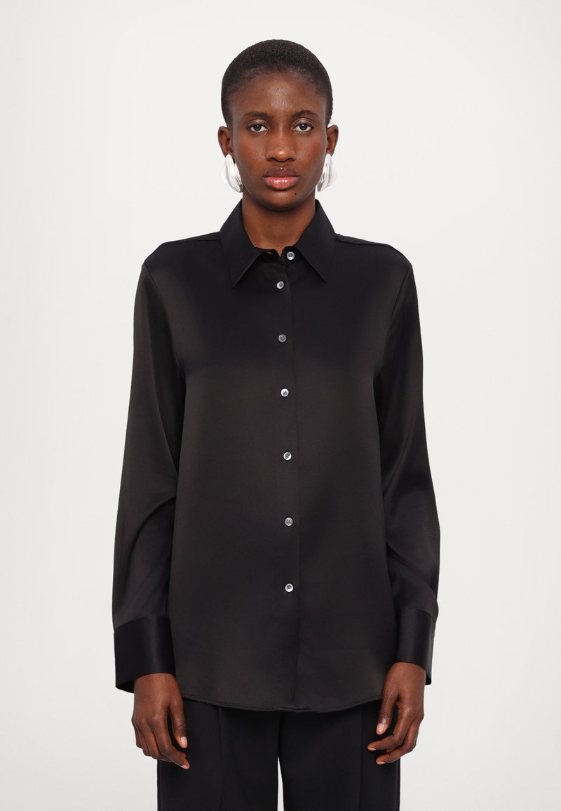 Chemise en satin noir avec des manches longues, un col, une patte de boutonnage à l'avant et des détails de boutons brillants. Texture lisse et coupe décontractée.
