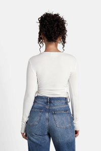 Top bianco a maniche lunghe con design aderente, legato in vita, abbinato a jeans blu a vita alta con tasche posteriori.