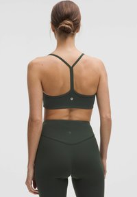 Sujetador deportivo de color verde oscuro con un diseño de espalda nadadora, que presenta tirantes finos y un detalle de logo en la parte posterior, combinado con leggings de talle alto a juego.