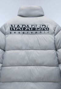 Ljust grå pufferjacka med hög krage och en svart tryckt logotyp på baksidan. Konstruerad med en quiltad, vadderad textur.