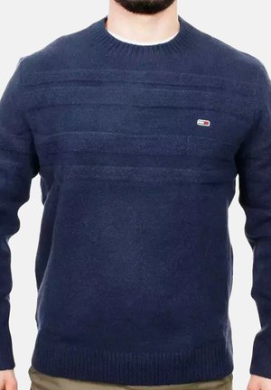 Mann trägt einen marineblauen Pullover mit Rundhalsausschnitt, dezenten horizontalen Streifen und einem kleinen rechteckigen Logo auf der linken Brust.