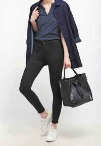 Blusa navy a pois, pantaloni neri slim-fit, sneakers bianchi e una borsa nera testurizzata con dettagli dorati.