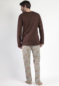Camisa de manga larga marrón combinada con pantalones de pijama marrones claros que presentan un patrón de Snoopy y acentos azules. Material de algodón suave, corte relajado.