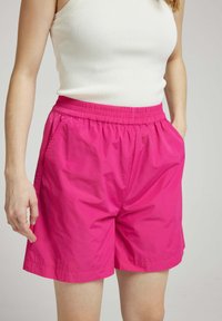 Shorts légers de couleur rose avec une taille élastique et des poches latérales. Texture lisse, longueur au genou et détails de coutures minimalistes.
