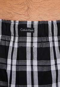 Schwarz-weiße Karomuster Boxer-Shorts mit einem elastischen Bund, der ein Calvin Klein Etikett zeigt, aus weichem Baumwollmaterial gefertigt.