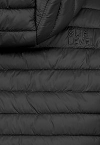 Schwarze Steppjacke mit horizontalem Quiltmuster, ausgestattet mit einem hohen Kragen und dem "SUB LEVEL"-Logo in schwarzer Stickerei auf dem Stoff.