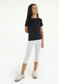 T-shirt à manches courtes bleu marine foncé assorti �à des leggings capri blancs et des baskets légères avec des accents crème et beige. Le modèle se tient les bras croisés.