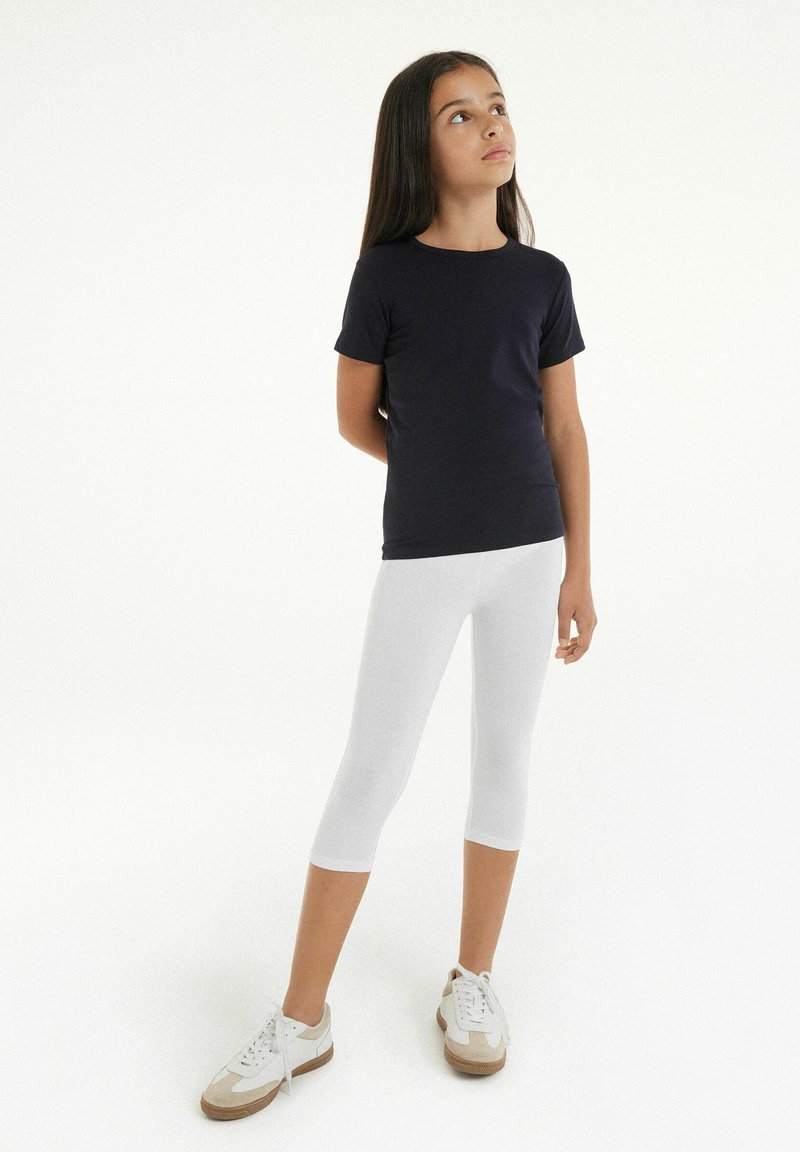 T-shirt à manches courtes bleu marine foncé assorti à des leggings capri blancs et des baskets légères avec des accents crème et beige. Le modèle se tient les bras croisés.
