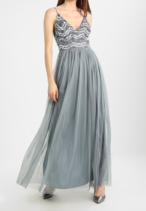 Femme portant une robe argentée sans manches avec un corsage à paillettes et une jupe fluide en tulle, assortie à des escarpins métalliques à bout pointu.