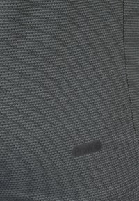 Tejido gris oscuro con un patrón texturizado, que presenta una pequeña etiqueta con el logo de ProW3B. El material parece duradero con detalles de estrías horizontales.
