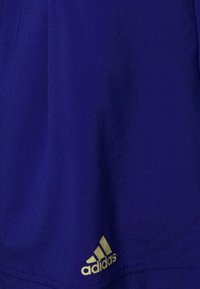 Camiseta deportiva morada hecha de una tela suave, con un logo dorado de Adidas en la esquina inferior derecha, y un diseño simple y sin adornos.