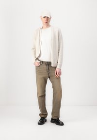Beige cardigan over a white t-shirt, paired with light brown jeans and black shoes. Accessories include a beige cap. Smooth texture.