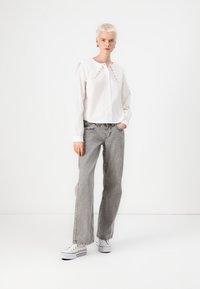 Hvit langermet skjorte med volangkrage, sammen med høyt liv grå jeans og hvite joggesko. Enkelt design, uformell passform.