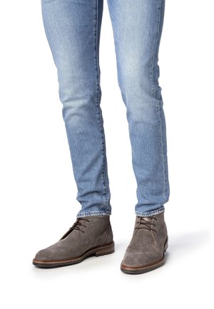 Bottines en daim gris avec bout arrondi, fermeture à lacets sur le devant et semelle en caoutchouc, associées à un jean slim bleu clair.