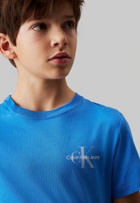T-shirt in cotone blu con collo a giro e stampa del logo bianco sul petto sinistro con la scritta "Calvin Klein Jeans." Texture morbida.