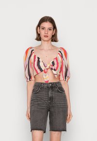 Blusa curta às riscas com mangas bufantes, apresentando um detalhe em nó na frente. Combinada com calções de ganga pretos desbotados de cintura alta.