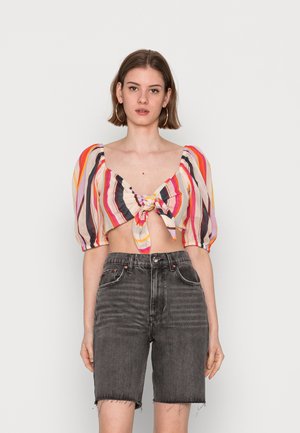 Blusa curta às riscas com mangas bufantes, apresentando um detalhe em nó na frente. Combinada com calções de ganga pretos desbotados de cintura alta.