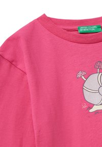 Růžové bavlněné tričko s kulatým výstřihem, s grafickým designem kulatého objektu a hub. Štítek hlásí "United Colors of Benetton."