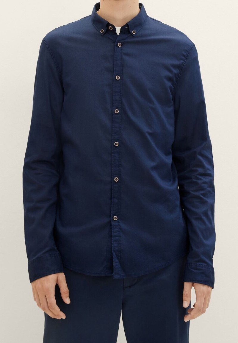 Mörkblå långärmad skjorta med krage, som har knäppning fram, manschettdetaljer och en slät tygtextur.