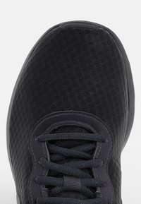 Svart sportskor med mesh-ovandel, rund tå och svarta snören knutna i ett standard korsmönster.