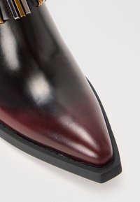 Chaussure en cuir à bout pointu dégradé de noir et bordeaux avec une semelle en caoutchouc noire et un détail de bride accentué en or près de la cheville.