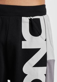 Black sweatpants with a large white graphic, gray side panels, and a black elastic waistband. Made from a soft cotton blend.