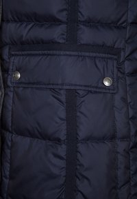 Giubbotto imbottito blu navy con texture trapuntata, tasca anteriore con chiusura a scatto e cinturino interno per regolazione o appeso.