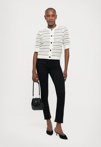 White short-sleeve cardigan with black horizontal stripes, button closure, paired with black fitted pants and a small black handbag.