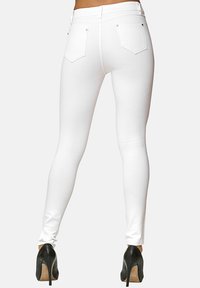 Jeans skinny bianchi con una texture liscia e design a cinque tasche, caratterizzati da accessori in tonalità dorata e una vita alta. Indossati con tacchi alti neri.