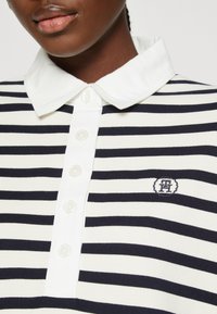 Polo w paski w kolorze granatowym i białym, z zapięciem na guziki, białym kołnierzykiem i małym haftowanym logo na piersi.