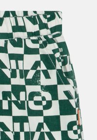 Shorts a quadretti verdi e bianchi con grandi lettere in blocco, dotati di una vita elasticizzata e cuciture a contrasto. Nessuna tasca visibile.