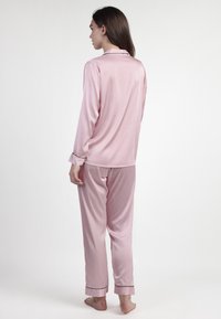 Conjunto de pijama de satén rosa que incluye una camisa de manga larga, un collar y puños en contraste. Los pantalones son de corte holgado y tienen una textura suave.