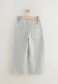 Gestreifte weit geschnittene Hosen hängen an einem Holzkleiderbügel. Sie haben einen weißen Hintergrund mit dünnen schwarzen vertikalen Streifen und zwei Gesäßtaschen.