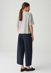 Grijze, gepersonaliseerde top met korte mouwen, gecombineerd met marineblauwe, wijde broeken. De outfit wordt afgemaakt met zwarte platte schoenen met een strikdetail.