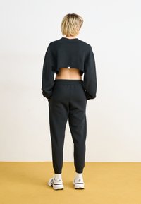 Svart avkortet hettegenser med høy krage og store ermer, kombinert med svarte joggebukser med elastiske mansjetter og midje.