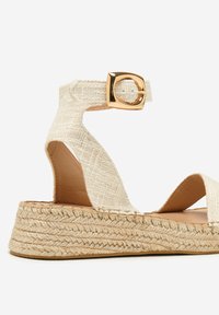 Kileespadrillesandal med øverste del i beige vævet stof, justerbar ankelrem med guldspænde og sål i jute-tov.