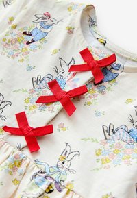 Katoenen jurk met een bloemenpatroon en geïllustreerde konijnen. Drie rode lintaccenten bij de halslijn en een geplooide zoom.
