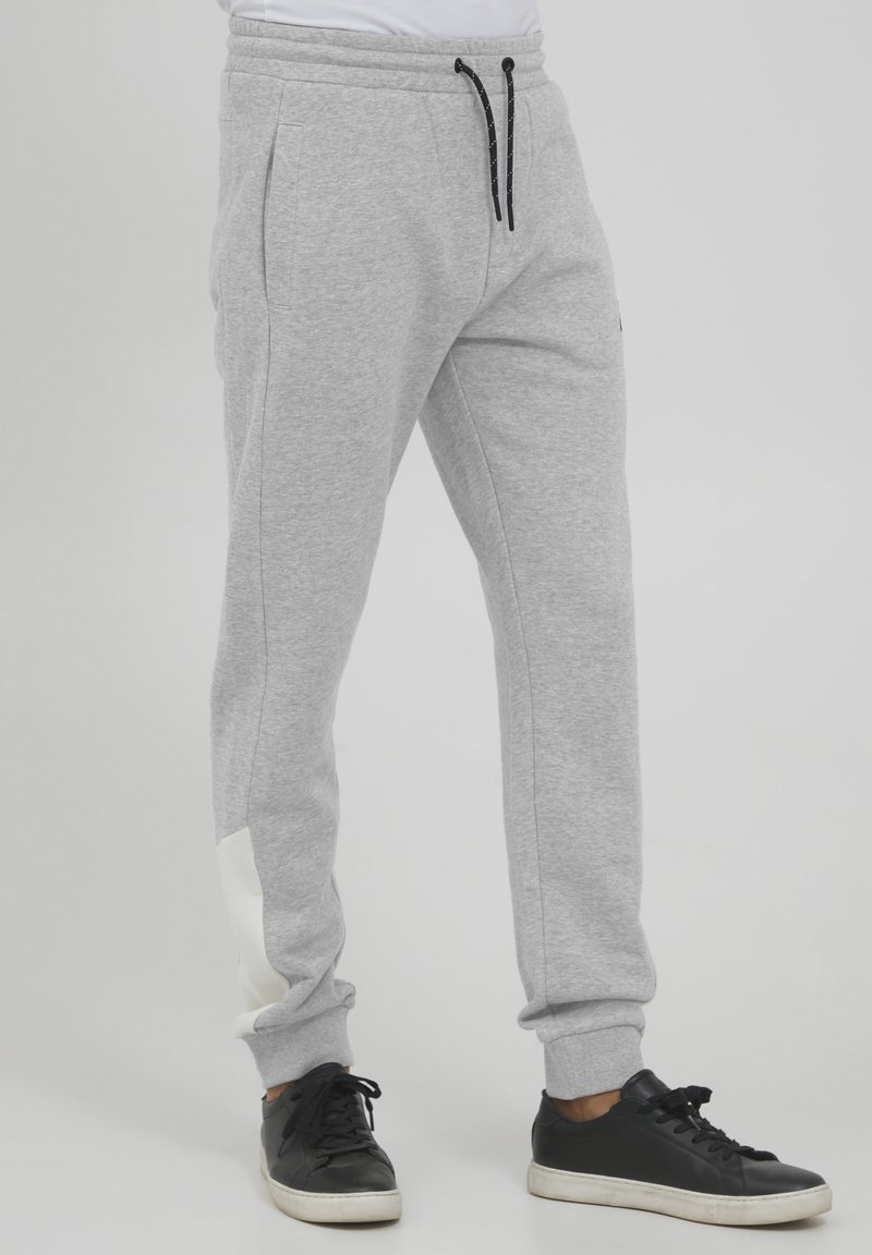 Graue Sweatshirt-Hose aus weichem Material mit einem elastischen Bund, schwarzem Kordelzug, seitlichen Taschen und einem weißen Akzent am Saum.
