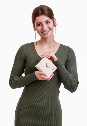 Compact beige wallet made of smooth synthetic material, featuring a metal accent and zip closure; held by a person in a ribbed green dress.