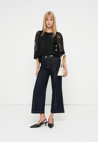 Czarna koronkowa bluzka z szerokimi rękawami, w połączeniu z ciemnoniebieskimi spodniami z wysokim stanem i szerokimi nogawkami. Uzupełniona małą białą torebką i czarnymi szpilkami.