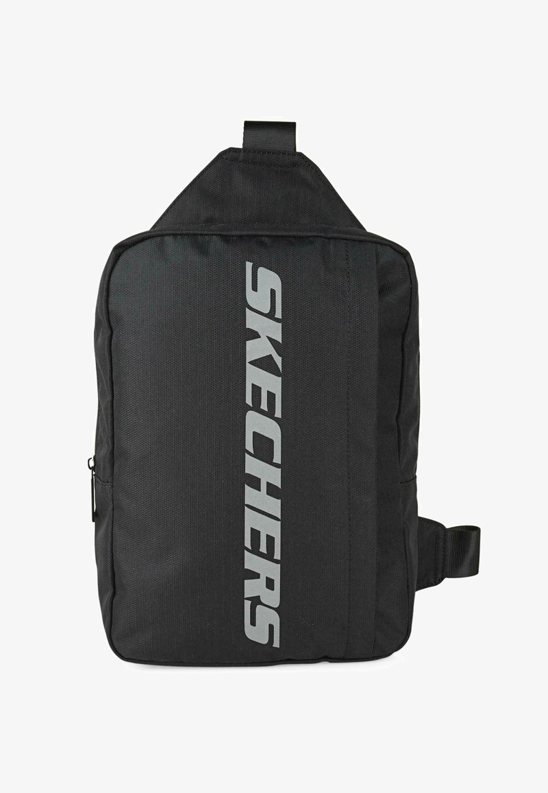 Mochila de tela negra con forma rectangular, que presenta un prominente logo gris de "SKECHERS" en posición vertical. Incluye un asa en la parte superior y una correa lateral.