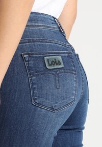 Tmavomodré denimové džínsy so slim fit strihom, s nášivkou značky Lois na zadnej vrecku a viditeľnými stehovými detailmi.