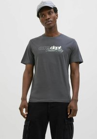 Grå bomulds T-shirt med korte ærmer og rund halsudskæring. Forsiden har trykt hvid tekst; iført sorte cargo bukser.