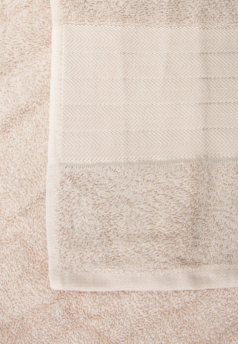 Beige Handtuch mit strukturiertem Frottiermaterial auf einer Seite und einem glatten, gemusterten Streifen auf der anderen, mit einem subtilen Fischgrätmuster.