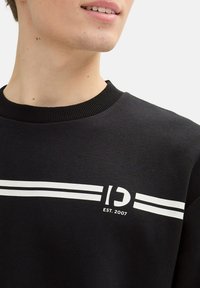 Sweatshirt nero con scollatura a costine, caratterizzato da strisce orizzontali bianche e un logo che include "D" e "EST. 2007." Texture morbida.